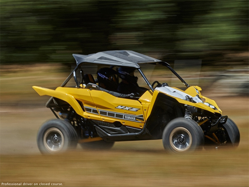 A yellow UTV cruising along a dirt road with a forest in the background